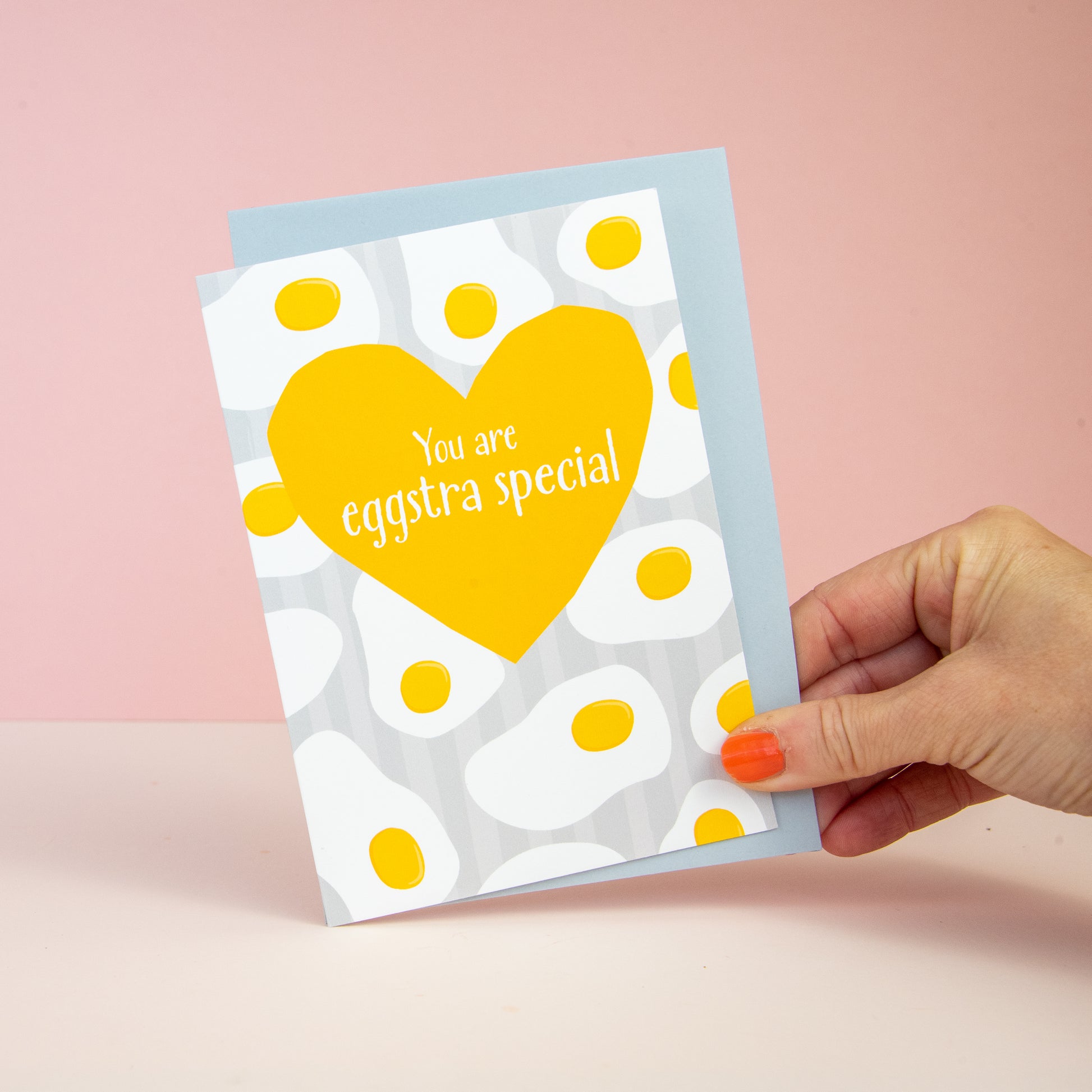 grey striped background with a pattern of fried eggs. a yellow heart and the wording your are eggstra special